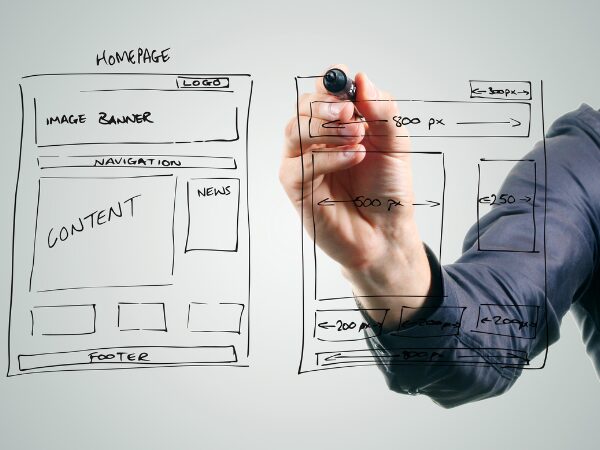 For the Website Design Setup and Hosting section. The image shows a person drawing a website wireframe on a transparent surface with a black marker. The wireframe outlines the layout of a homepage, including sections labeled "Logo," "Image Banner," "Navigation," "Content," "News," and "Footer." The drawing includes dimensions for different sections, such as "800 px" for the width of the banner and "250 px" for a side element. The person’s hand is visible holding the marker, and they appear to be actively sketching the layout. The overall scene conveys the process of planning and designing a website's structure.