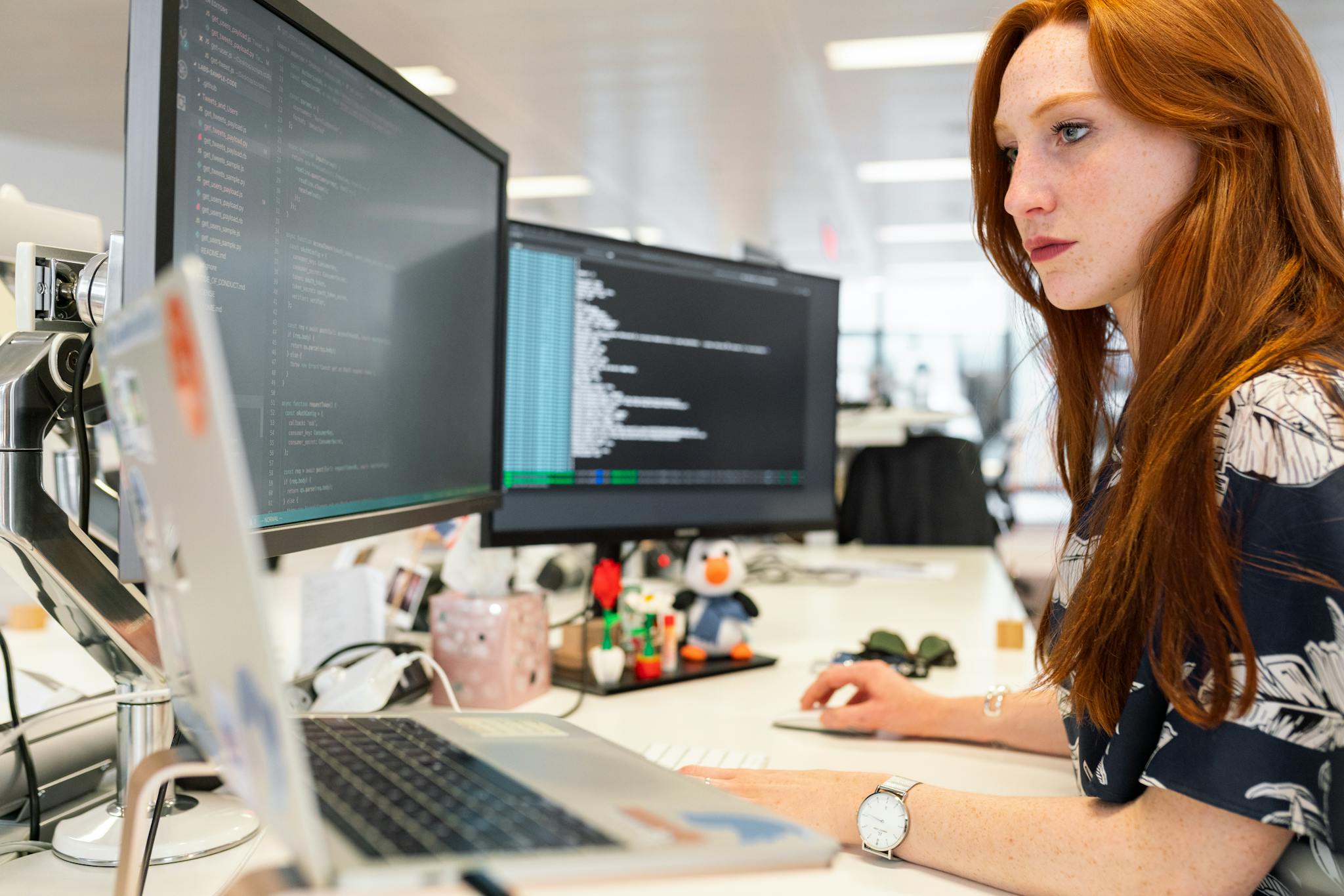 The image shows a woman with long red hair working at a desk with multiple computer monitors. For the website management section.